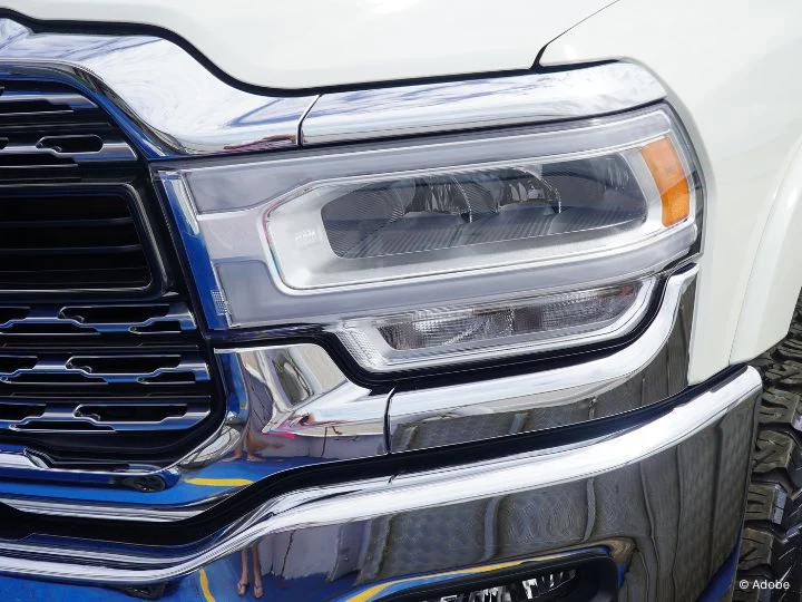 A close-up of the driver's side headlight of a white Ram vehicle.